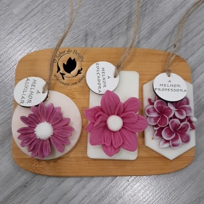 Três placas decorativas com flores rosa e etiquetas com texto em português sobre chão cinza.