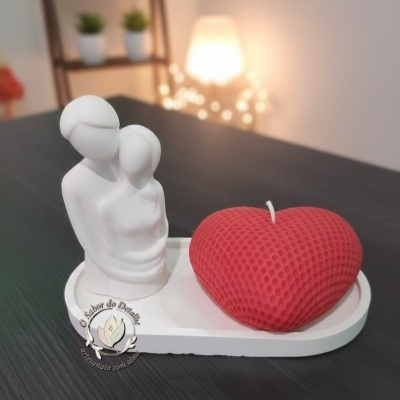 Vela vermelha em forma de coração com textura, escultura branca de casal e base branca sobre mesa preta