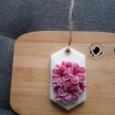 Vela decorativa branca hexagonal com flores rosa e fio rústico sobre tábua de madeira e tecido cinza