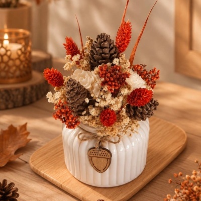 Arranjo decorativo em vaso branco com pinhas e flores secas em tons laranja e bege