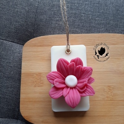 Placa branca com flor rosa em relevo e cordão de suspensão sobre superfície de madeira clara