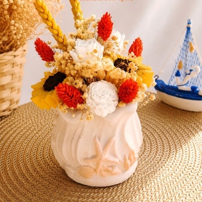 Arranjo floral seco em vaso cerâmico branco com relevos de estrela-do-mar e conchas
