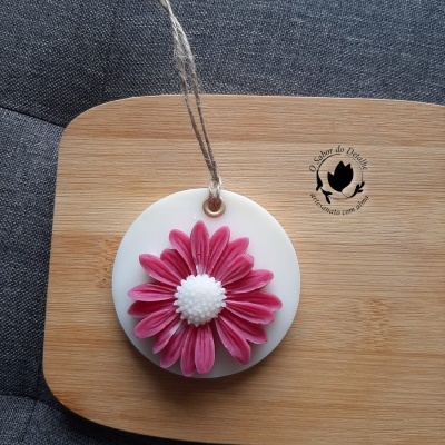 Difusor aromatizador branco com flor rosa pendurado em tábua de madeira