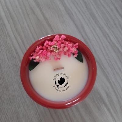 Vela artesanal cremosa num recipiente vermelho com flores rosas decorativas