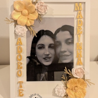 Moldura branca decorada com flores douradas e brancas e fotografia de duas mulheres