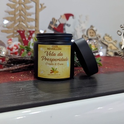 Vela da Prosperidade em pote preto com rótulo amarelo e decoração natalícia em fundo