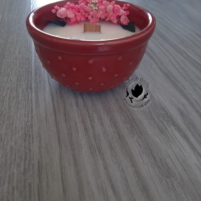 Vela branca com pavio de madeira numa taça de cerâmica vermelha decorada com flores cor-de-rosa