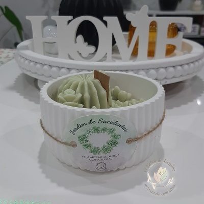 Vela decorativa branca com moldes verdes de cactos e suculentas em recipiente canelado branco.