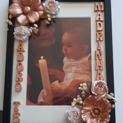 Moldura preta com decoração de flores e letras cobre com foto de bebé segurando vela.