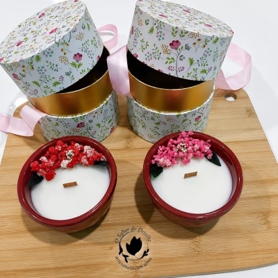 Duas velas decorativas com flores secas e caixas florais colocadas sobre uma base de madeira