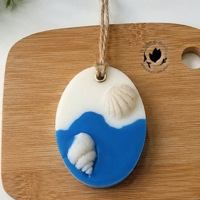 Ornamento oval branco e azul com conchas e cordão sobre tábua de madeira