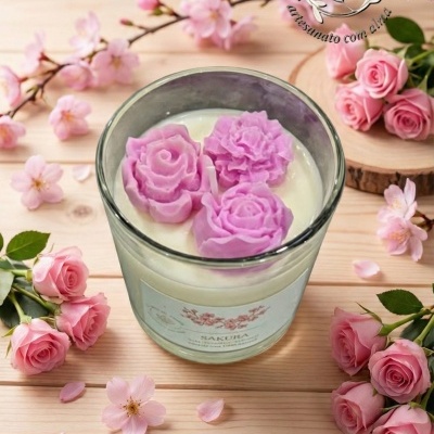 Vela perfumada em copo de vidro com decoração de flores cor de rosa e flores naturais ao redor