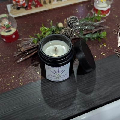 Vela em frasco preto com etiqueta de lavanda e alecrim, sobre superfície brilhante com decoração natalícia