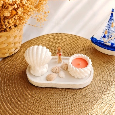Conjunto decorativo com vela, conchas, garrafa pequena, flores secas em vaso de vime e barco azul