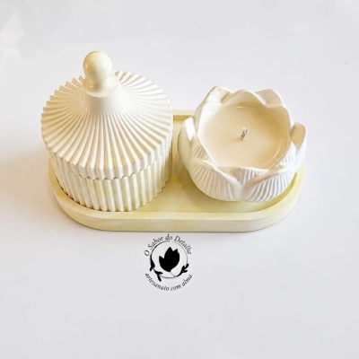 Vela branca em recipiente de cerâmica em forma de flor e pote canelado de cerâmica numa base oval clara