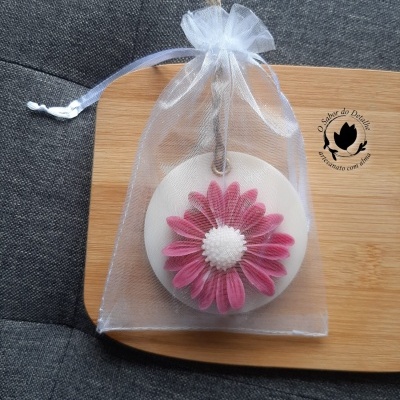 Placa decorativa branca com flor rosa embalada em saco transparente sobre madeira e tecido cinzento