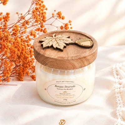 Vela artesanal Bosque Dourado com tampa de madeira decorada e flores secas laranja.
