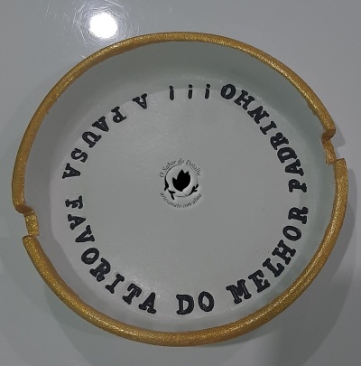 Parte superior de uma peça cerâmica branca com borda dourada e texto preto em círculo