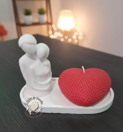 Vela vermelha em forma de coração com textura, escultura branca de casal e base branca sobre mesa preta