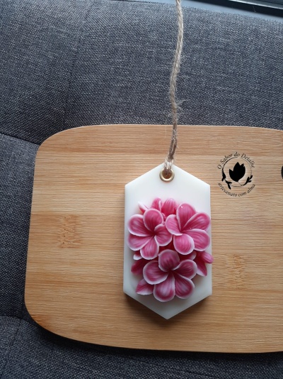 Vela decorativa branca hexagonal com flores rosa e fio rústico sobre tábua de madeira e tecido cinza