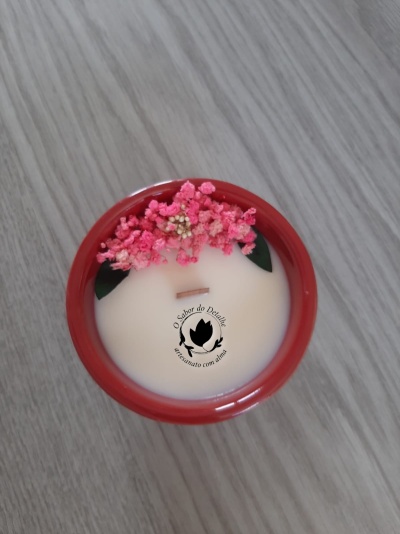 Vela artesanal cremosa num recipiente vermelho com flores rosas decorativas