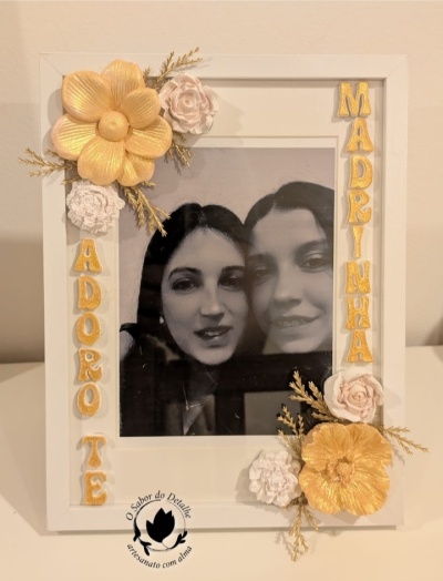Moldura branca decorada com flores douradas e brancas e fotografia de duas mulheres