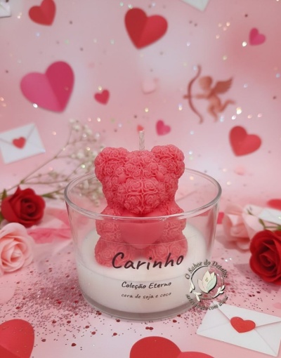 Vela com urso cor-de-rosa de rosas em copo transparente com texto carinhoso num fundo rosa com corações e flores.