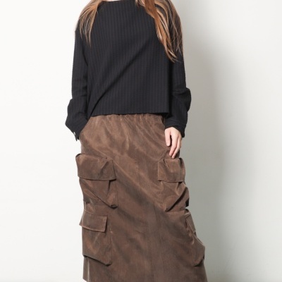 Mulher a vestir camisola preta, saia castanha com bolsos grandes, meias vermelhas e sapatilhas castanhas.