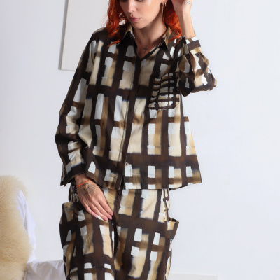Mulher com cabelo ruivo veste conjunto com padrão geométrico castanho, bege e branco em ambiente interior