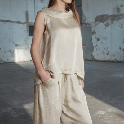 Mulher com conjunto creme acetinado de blusa sem mangas e calças largas, em ambiente industrial