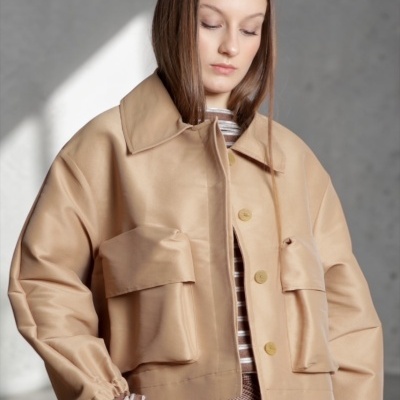 Casaco bege curto com bolsos grandes e botões, usado por uma mulher com camisola riscada por baixo.