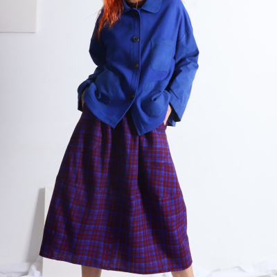 Mulher com casaco azul e saia xadrez azul e vermelho em fundo branco