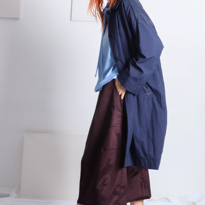 Mulher com casaco azul marinho, camisola azul clara, saia castanha, meias cinzentas e sapatos pretos em fundo branco