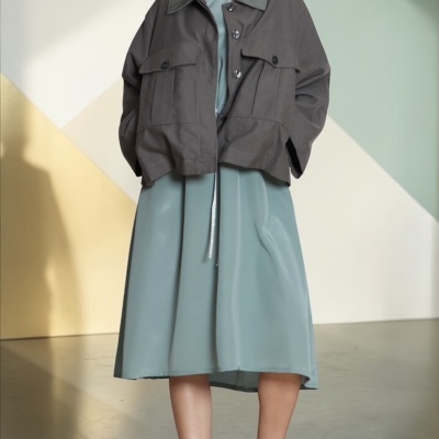 Mulher com casaco cinza, vestido azul acinzentado e sandálias verdes de plataforma