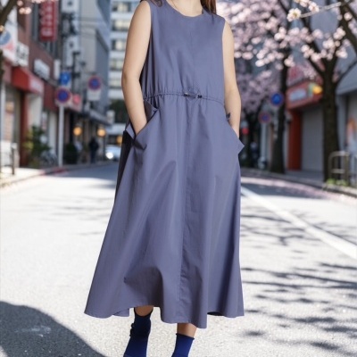 Mulher a usar vestido cinza-azulado sem mangas em rua urbana com árvores floridas.