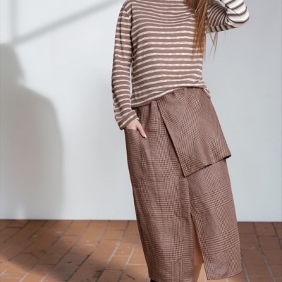 Mulher com camisola de riscas e saia xadrez castanha em chão de tijoleira