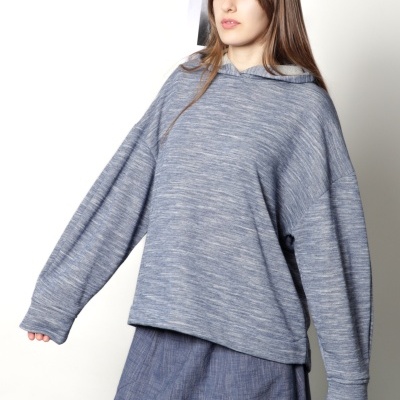 Sweatshirt cinzenta e saia azul usadas por mulher com cabelo castanho.