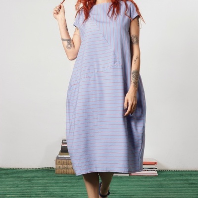 Vestido azul claro com riscas finas rosa usado por mulher com cabelo ruivo e tatuagens em ambiente interior