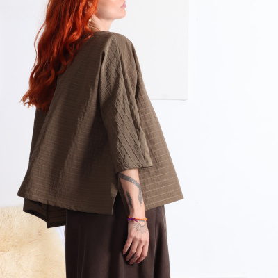 Mulher ruiva de blusa castanha com textura canelada em fundo branco
