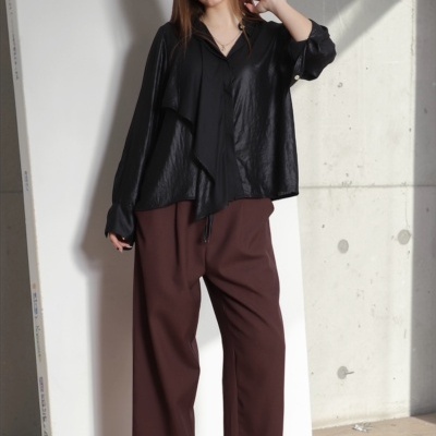 Mulher vestindo camisa preta brilhante, calças castanhas largas e sapatos pretos de salto