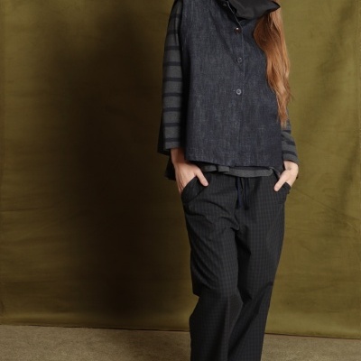 Mulher veste camisola riscas, colete azul, calças xadrez e sapatilhas cinzentas em fundo castanho.