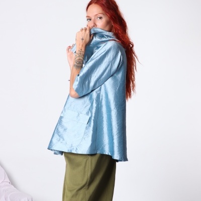 Pessoa a usar t-shirt azul brilhante com bolso e calças verdes em fundo branco