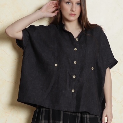 Blusa preta de manga curta com botões e saia xadrez preta em fundo de parede bege