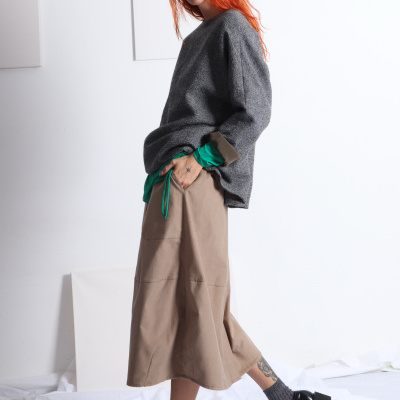 Modelo feminina vestindo roupa casual com suéter cinza e saia bege.