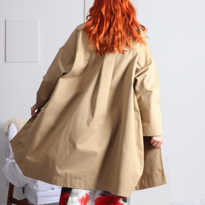 Casaco bege com saia estampada e cabelo ruivo visto de trás, em ambiente interior.