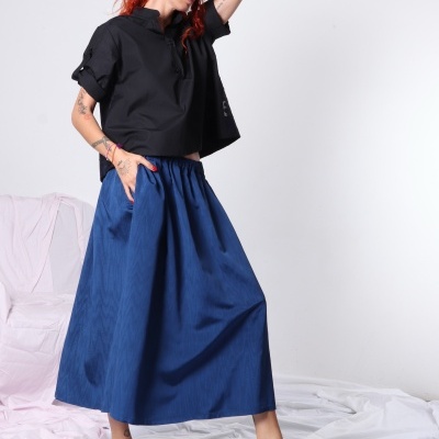 Mulher com camisa preta, saia azul longa e sandálias pretas