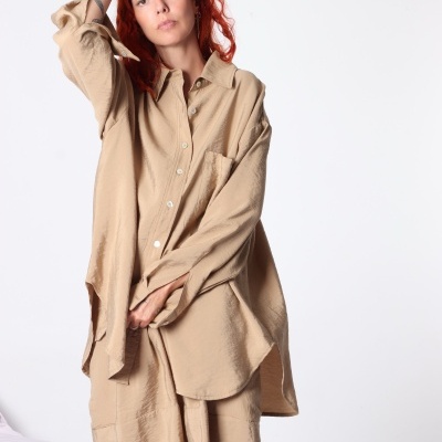 Conjunto bege de camisa e calças com botões e bolso, em fundo branco.
