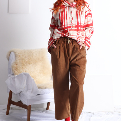 Mulher com blusa creme e vermelha xadrez, calças castanhas, meias vermelhas, botas castanhas e cadeira com manta peluda