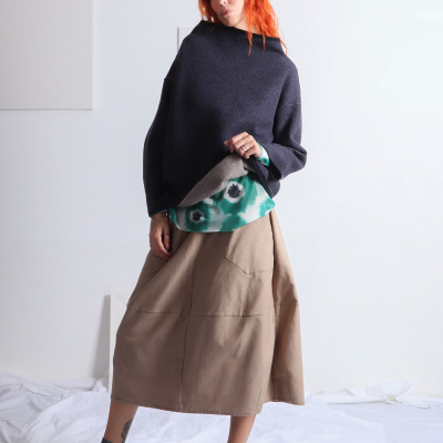 Mulher com camisola cinza, blusa verde e saia bege em fundo branco