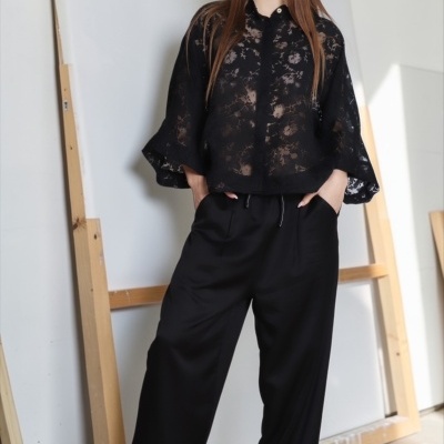 Mulher com roupa preta e sandálias verdes em ambiente com telas e molduras de madeira.